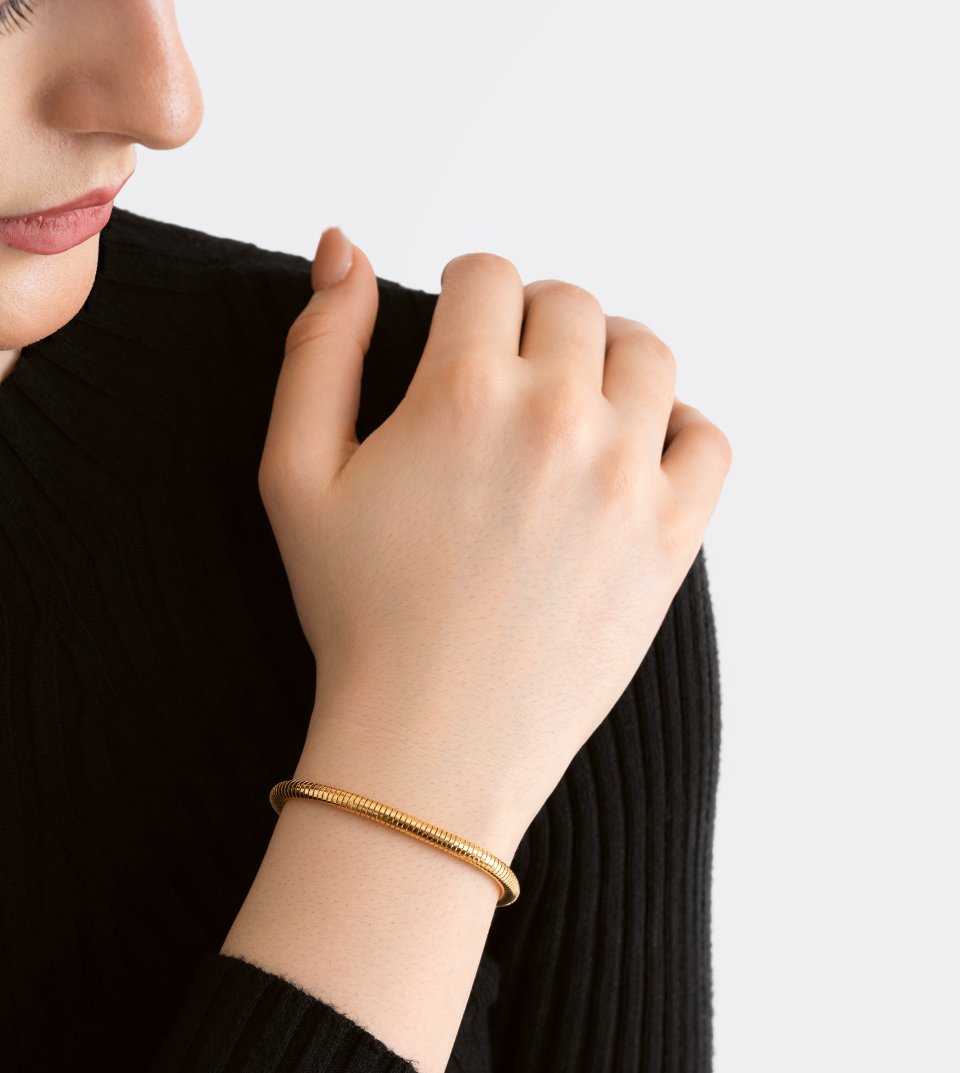 Close-up of a person wearing a gold bracelet on a plain background