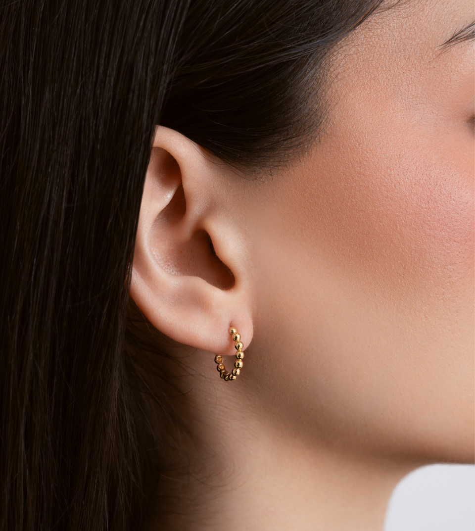 Gold hoop earring worn by a person with dark hair.